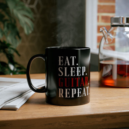Black mug with 'Eat. Sleep. Guitar Repeat.' text on a wooden surface.