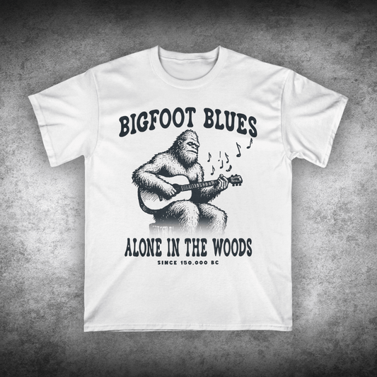 White t-shirt with a graphic of a bigfoot playing guitar and text on a textured gray background