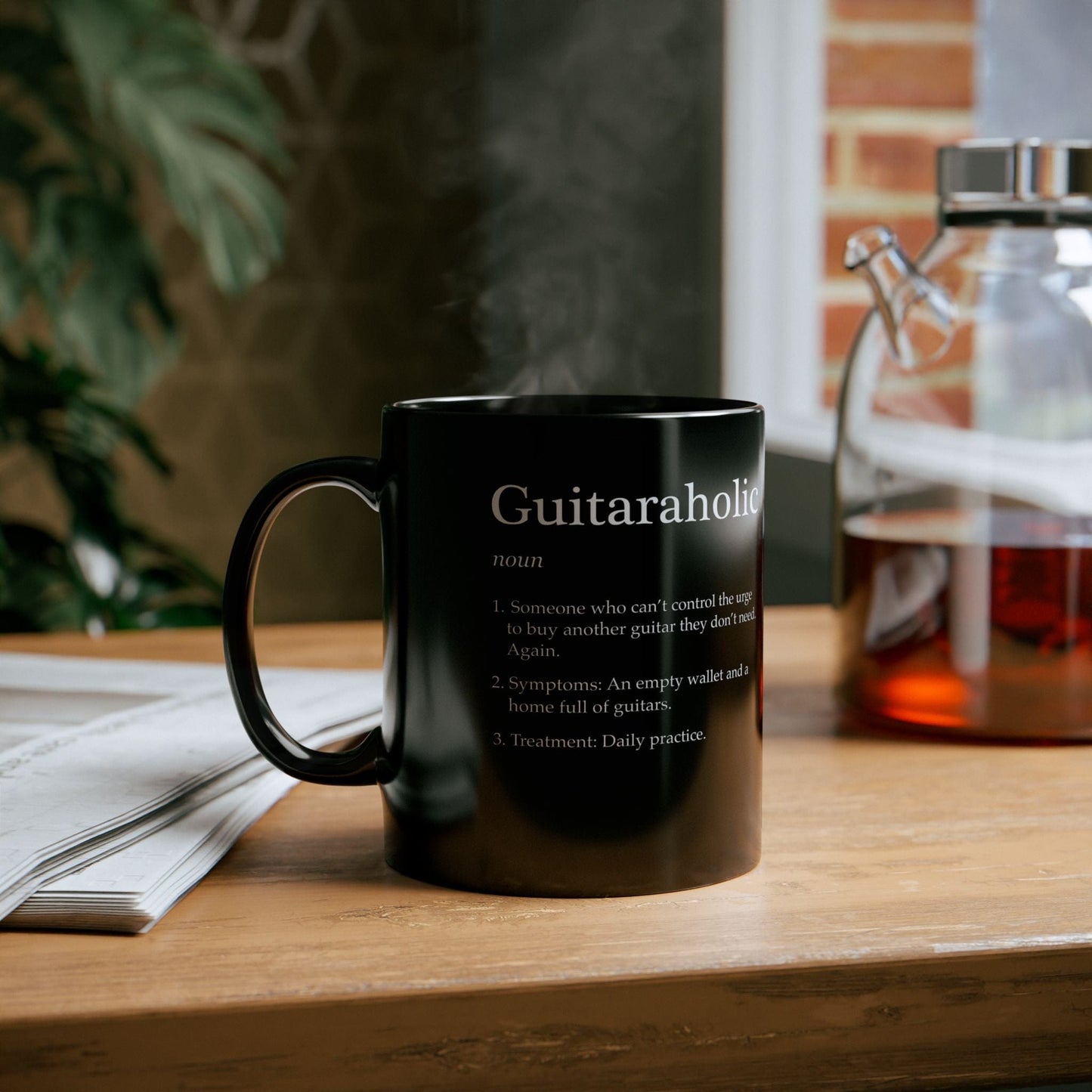 Black mug with 'Guitaraholic' definition on a wooden surface with a blurred background