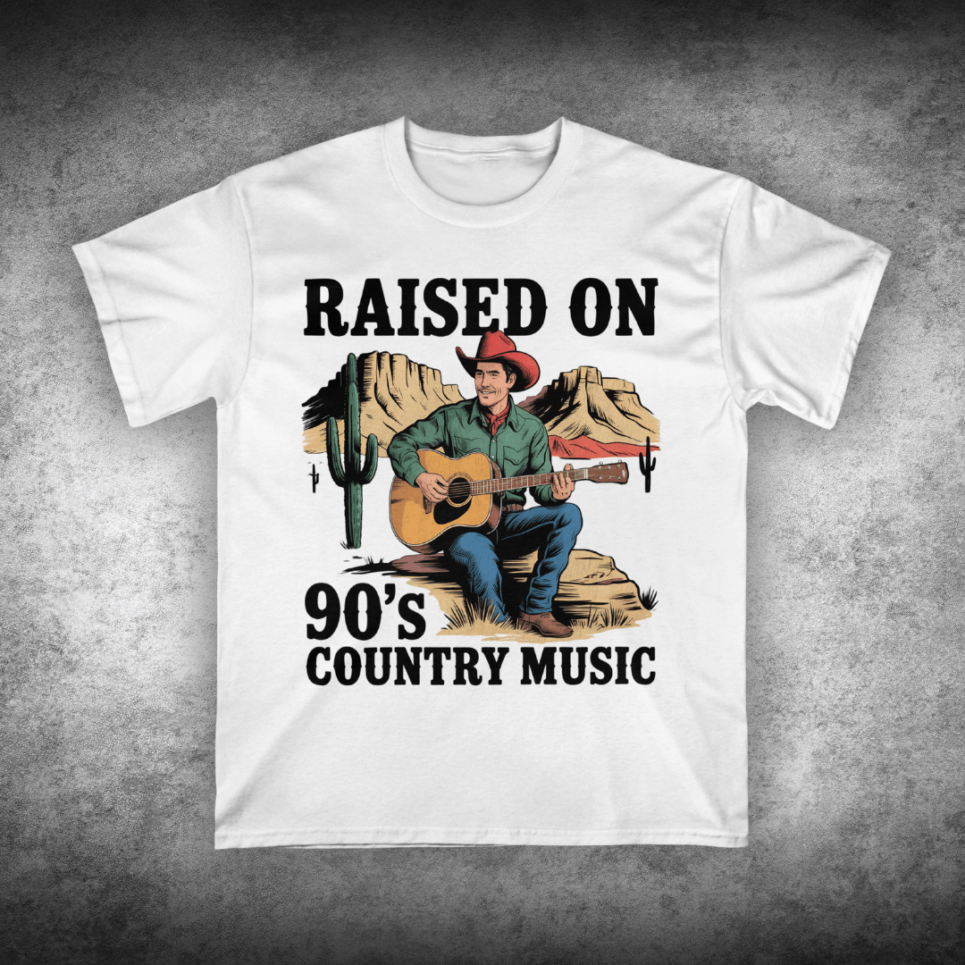 White t-shirt with a graphic of a cowboy playing guitar and text 'Raised on 90's Country Music' on a textured gray background.